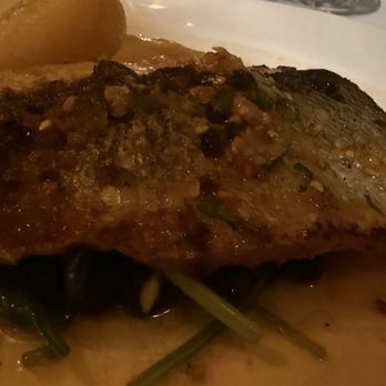 Sette - Merluzzo Alla Piastra Wild Icelandic Cod, (or Snapper) Cast Iron Seared, Sicilian Cherry Tomato Ratatouille - A fish fillet with a seasoned, crispy skin is plated with greens and lemon wedges, likely from a restaurant meal. - Italian Near Me - Bernardsville, New Jersey