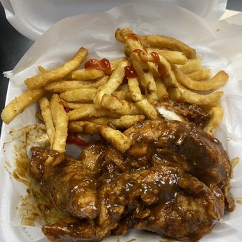 Peppajak - Jamaican Jerk Chicken and French Fries. - French fries with ketchup and a chicken wing covered in brown sauce are placed in a foam takeout container lined with paper. The fries are golden and slightly crispy, with some ketchup drizzled on top. The chicken wing appears saucy and cooked, with the sauce coating the meat. The container is open, showing the food inside, and the background is dark and out of focus. - Seafood Near Me - Riverview, Florida
