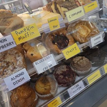 Cath Coffee - A bakery display case contains muffins and baked goods labeled with flavors like pumpkin, blueberry, and pecan, along with slices of cake. - Coffee & Tea Near Me - Indianapolis, Indiana