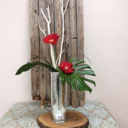 Burlington Flowers & Formalwear - A silver pre-lit mercury glass vase perfect for events. Large monsters leaves, red, gerbera daisy's, mitsumata branches.