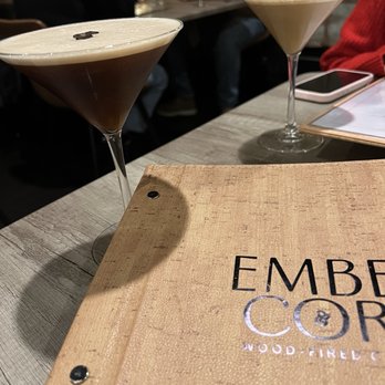 Ember & Cork - Espresso Martini - Two espresso martinis in cocktail glasses are on a wooden table at Ember & Cork, a restaurant with a wood-fired menu, with a menu and a smartphone nearby. - Seafood Near Me - Schenectady, New York