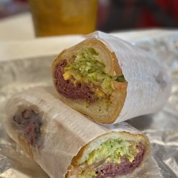 Moe's Deli & Grocery - Pastrami Sandwich on a whole wheat hero with lettuce, tomatoes, and mustard.
