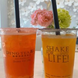 Passion fruit green tea - Two fruit teas in clear cups with black straws are placed on a table, with a floral background and a decorative wall.