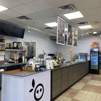 Teamoji - A cafe interior features a counter with menu boards hanging above, beverage machines, and a refrigerator, with a tiled floor and ceiling lights. - Bubble Tea Near Me - Woburn, Massachusetts
