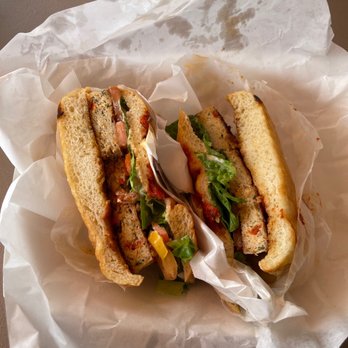 Herm's Palace - Chicken Caesar burger - Two sandwiches with bread, lettuce, tomato, and various fillings are shown in a paper wrapper on a flat surface. The sandwiches are partially eaten, revealing the ingredients inside. The image focuses on the food, with no visible restaurant or storefront context. - American Near Me - Skokie, Illinois