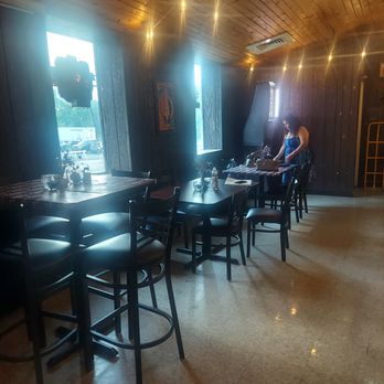 La Opera - A woman in a blue dress stands near a table in a restaurant with wooden walls and ceiling, illuminated by string lights and natural light from windows. - Bars Near Me - Waukegan, Illinois