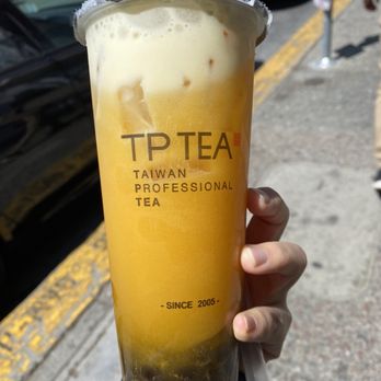 TP TEA - Passion fruit green tea w/ boba - A large, transparent cup of passion fruit green tea with black tapioca pearls at the bottom, branded with TP TEA, Taiwan Professional Tea, established in 2005. The drink has a foamy top and is held outdoors on a sidewalk with parked cars and a street scene in the background. - Coffee & Tea Near Me - Berkeley, California