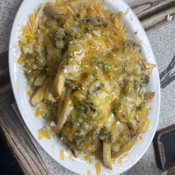 The Crane Cafe - Green Chile cheese fries - A white oval plate holds cheese fries with melted cheese, jalapeños, and possibly other toppings, served on a table. - Mexican Near Me - Lemitar, New Mexico