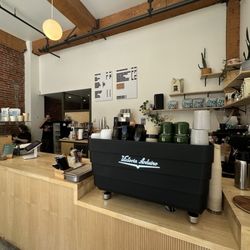 A clean, minimalist counter with warm wood tones, exposed brick, and a sleek espresso machine