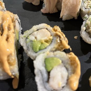 Kusshi - Inside the Fenton ($20) - Sushi rolls with avocado and seafood filling are displayed on a black plate, topped with sauce and garnishes. - Sushi Bars Near Me - Silver Spring, Maryland