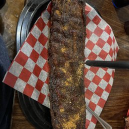 Ribs - A smoked meat rack, possibly ribs, is placed on a tray lined with red and white checkered paper, topped with seasoning and spices.
