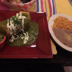 Chicken chimichangas covered in green sauce with a side of rice and beans.