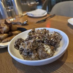 Crispy Cauliflower - amazing! - A white bowl contains crispy cauliflower florets topped with pine nuts, placed on a wooden table in a restaurant setting.