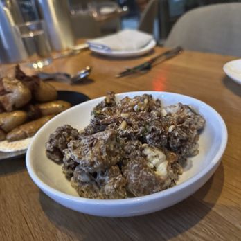 Chloe - Crispy Cauliflower - amazing! - A white bowl contains crispy cauliflower florets topped with pine nuts, placed on a wooden table in a restaurant setting. - New American Near Me - Washington, DC, District of Columbia