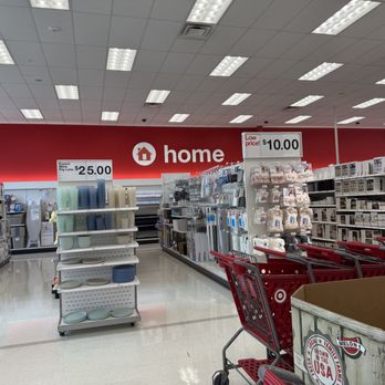 Target - The image shows an indoor Target store aisle dedicated to home products, with shelves stocked with various household items. Signage indicates prices such as $25.00 and $10.00. Several red shopping carts are positioned in the aisle, and a Target shopping cart with a Melon sticker is visible in the foreground. The ceiling features a grid of fluorescent lights, and the wall in the background displays a large red Target logo with the word 'home' next to it. - Department Stores Near Me - Skokie, Illinois