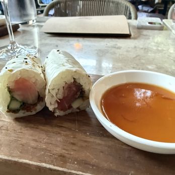 Uchi Austin - Tuna hand roll - Two sushi rolls with rice, fish, and vegetables are placed on a wooden board, accompanied by a bowl of dipping sauce, in a restaurant setting. - Sushi Bars Near Me - Austin, Texas