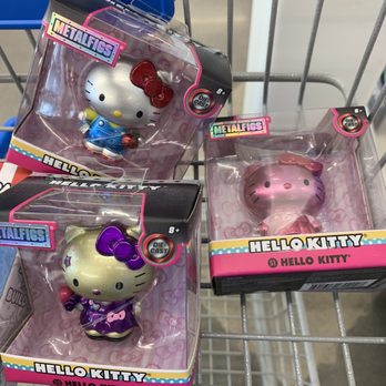 Five Below - Collectible Hello Kitty - Three Hello Kitty collectible figurines are displayed in their original packaging on a shopping cart. Each figurine features Hello Kitty in different outfits and colors, with two in metallic finishes and one in a gold tone. The packaging indicates they are part of the Metalfigs series and are suitable for ages 8 and up, with die-cast construction. The figurines are positioned in a retail environment, likely a store that sells toys or collectibles. - Discount Store Near Me - Surprise, Arizona