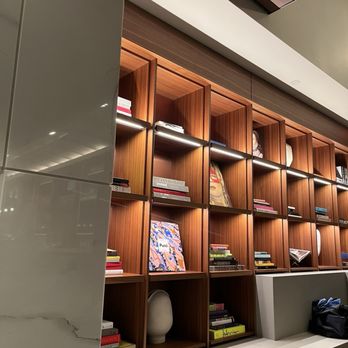 Kestra - Decor - A tall wooden bookshelf with multiple compartments, filled with books and decorative objects, is set against a wall in a contemporary space. - New American Near Me - Boston, Massachusetts
