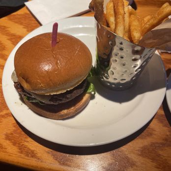 Glory Days Grill - Happy hour Mushroom swiss burger $7.99 - A cheeseburger with lettuce and a beef patty is served with French fries in a metal container on a white plate. - American Near Me - Frederick, Maryland