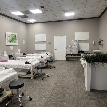 Relax Spa - Table message area - A treatment room with multiple beds, stools, and medical equipment, featuring neutral-colored walls and ceiling tiles. - Massage Near Me - Schaumburg, Illinois