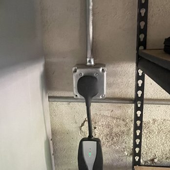 Elevation Electric - Nema 14-50 outlet - A Nema 14-50 outlet is mounted on a wall with a charging cable plugged in, in an industrial or garage setting. - Electricians Near Me
