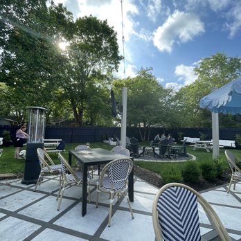 Something Splendid - An outdoor seating area with tables and chairs, a fire pit, and a blue fence surrounds the space, with trees and a partly cloudy sky overhead. - Gift Shops Near Me - Westfield, Indiana
