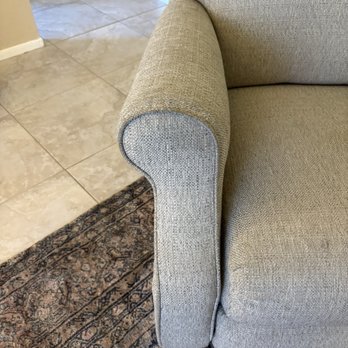 Coconut Cleaning - A beige fabric armrest of a sofa is shown, with a tiled floor and a patterned rug in the background. - Carpet Cleaning Near Me - Chandler, Arizona
