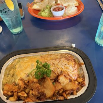 Pantry Restaurant - Breakfast burrito - A baked casserole dish featuring melted cheese on top, roasted potato chunks, and a garnish of parsley, served in a black-rimmed container. The dish appears hot and ready to eat, with a golden-brown cheese layer and crispy potato pieces. - Breakfast & Brunch Near Me - Santa Fe, New Mexico