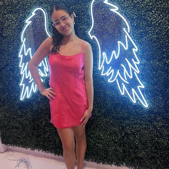 El Sitio Bar & Grill - a woman posing in front of a neon angel sign - Venezuelan Near Me - Miami, Florida