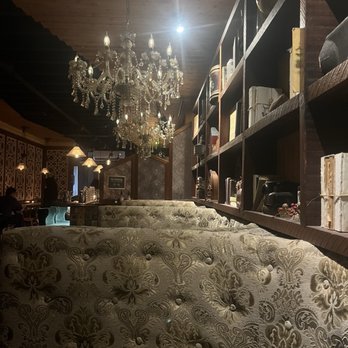 The Attic Oyster & Cocktail Bar - Seating below chandelier and shelving with books, trinkets and miscellaneous ornaments. - Cocktail Bars Near Me - Flushing, New York