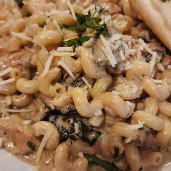 Patty B's - A bowl of pasta with a creamy sauce, topped with grated cheese and chopped herbs, featuring mushrooms and pasta shells. The dish appears to be served in a restaurant setting, with a dark wooden table visible in the background. - Italian Near Me - Dover, New Hampshire