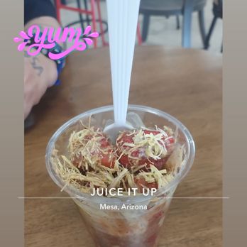 Juice Queen’s - Dubai Strawberry Cup. This place is delicious. - A dessert in a clear plastic cup contains strawberries, shredded toppings, and a white straw, placed on a wooden table at Juice Queen’s in Mesa, Arizona. - Juice Bars & Smoothies Near Me - Mesa, Arizona