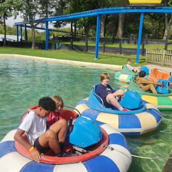 Little Amerricka - Kids are seated in colorful bumper boats on a water attraction at a park, with trees and a blue canopy overhead. - Amusement Parks Near Me - Marshall, Wisconsin