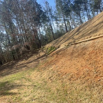 Ndeed Scapes - a dirt hill with a tree line in the background - Landscaping Near Me
