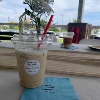 Coffee Malem - Iced latte - An iced latte in a clear plastic cup with a red straw, placed on a table with a blue napkin, at a cafe with outdoor seating. - Coffee & Tea Near Me - Cherry Hill, New Jersey