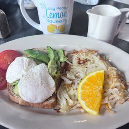 Avocado toast with two poached eggs, sliced avocado, sliced tomato, hashbrowns, orange slice, and coffee. Avocado toast with two poached eggs, sliced avocado, sliced tomato, hashbrowns, orange slice, and coffee.