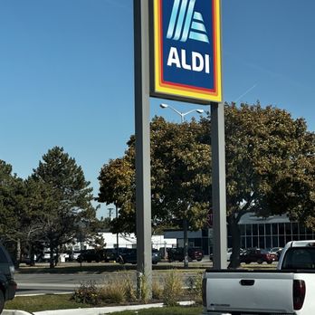 ALDI - a car parked in front of a aldi store - A large outdoor sign with the ALDI logo is visible in a parking lot, with trees and parked cars in the background. - Grocery Near Me - Roseville, Michigan