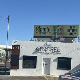 Building - A white building with black window frames and signage for The Coffee Builders and Simply Spiked drinks, located on a street with parked cars.