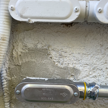 The Electric Connection - Image shows two electrical meters mounted on a textured wall, with conduit pipes connected to them, in an outdoor or utility area. - Electricians Near Me - Tujunga, California