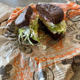 Veggie on rye - A sandwich with lettuce, mayonnaise, and meat on dark bread, cut in half, placed on branded paper from Schlotzsky's.