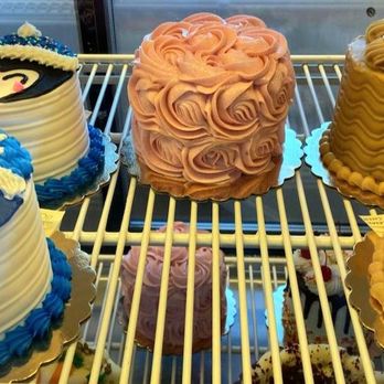 Smallcakes A Cupcakery - Assorted cakes with colorful frosting and decorative designs are shown in a bakery display case, including character-themed and textured cakes. - Bakeries Near Me - Albuquerque, New Mexico