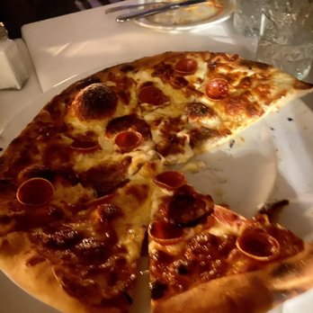 Flavio Restaurant DC - Pepperoni Pizza with white sauce - A pizza with pepperoni and sausage toppings on a white plate, served at a restaurant table with glasses of ice water and utensils. - Italian Near Me - Washington, DC, District of Columbia