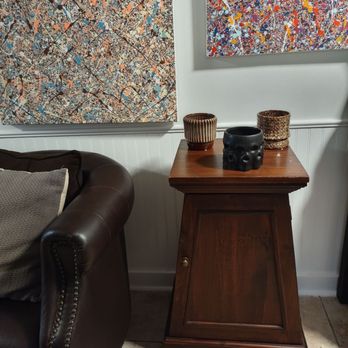 Ultimate Treasures - A wooden side table with three decorative pots is positioned beside a leather sofa in a room with abstract artwork on the wall. - Antiques Near Me - Downers Grove, Illinois