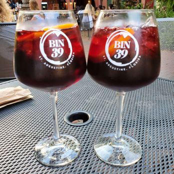 Bin 39 - Housemade Sangria - Two glasses of housemade sangria with ice and fruit sit on a metal table at Bin 39, a wine bar and bistro in St. Augustine, FL, with outdoor seating and a lively atmosphere. - Wine Bars Near Me - St. Augustine, Florida