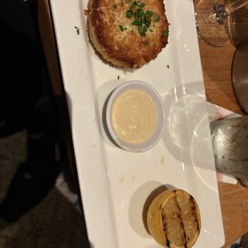 Seasons 52 - Crab cake of the highest quality! Oh so good! - A white rectangular plate holds a golden-brown crab cake garnished with chopped chives, a lemon half with grill marks, and a small cup of creamy dipping sauce. - New American Near Me - Albuquerque, New Mexico