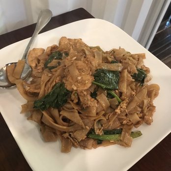 Paste Thai - Pad si ew - A serving of pad si ew, featuring wide rice noodles, cooked greens, and meat, presented on a white square plate. - Thai Near Me - Davis, California