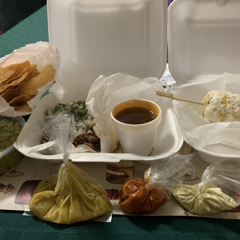 From Left to Right: Guacamole with chips, Birria QuesaTaco, consomé and elote. At the front, different small baggies of hot sauces. From Left to Right: Guacamole with chips, Birria QuesaTaco, consomé and elote. At the front, different small baggies of hot sauces.