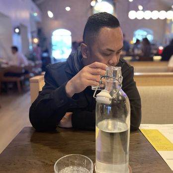 Bulevar Mexican Kitchen - A man in a black jacket is drinking water from a glass pitcher at a restaurant table, with a menu and glass in view. - Mexican Near Me - Austin, Texas