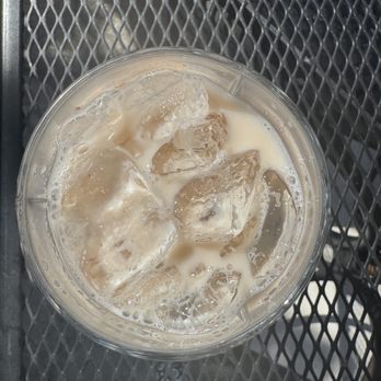 Zinnia - Top view of iced Masala Chai -- soo refreshing! - A clear plastic cup filled with iced Masala Chai, containing milk, ice cubes, and tea, placed on a metal mesh table. - Cocktail Bars Near Me - Silver Spring, Maryland