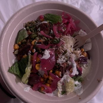 CAVA - Grain bowl with grilled chicken.  Tye hit honey chicken is also very good. - A disposable bowl contains a grain bowl with grilled chicken, rice, corn, lettuce, pickled onions, and drizzled sauces, with a fork. - Mediterranean Near Me - Newington, Connecticut